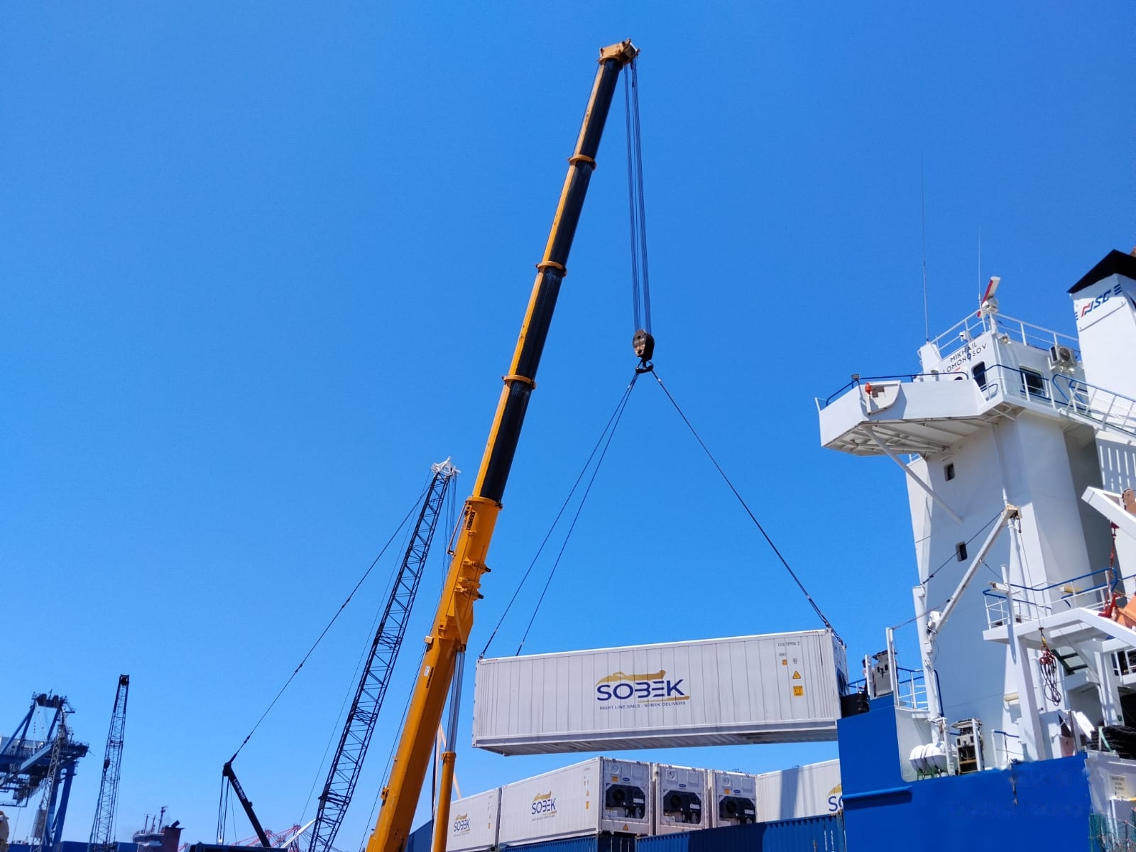 Mobile crane lifting a container beside a ship bridge