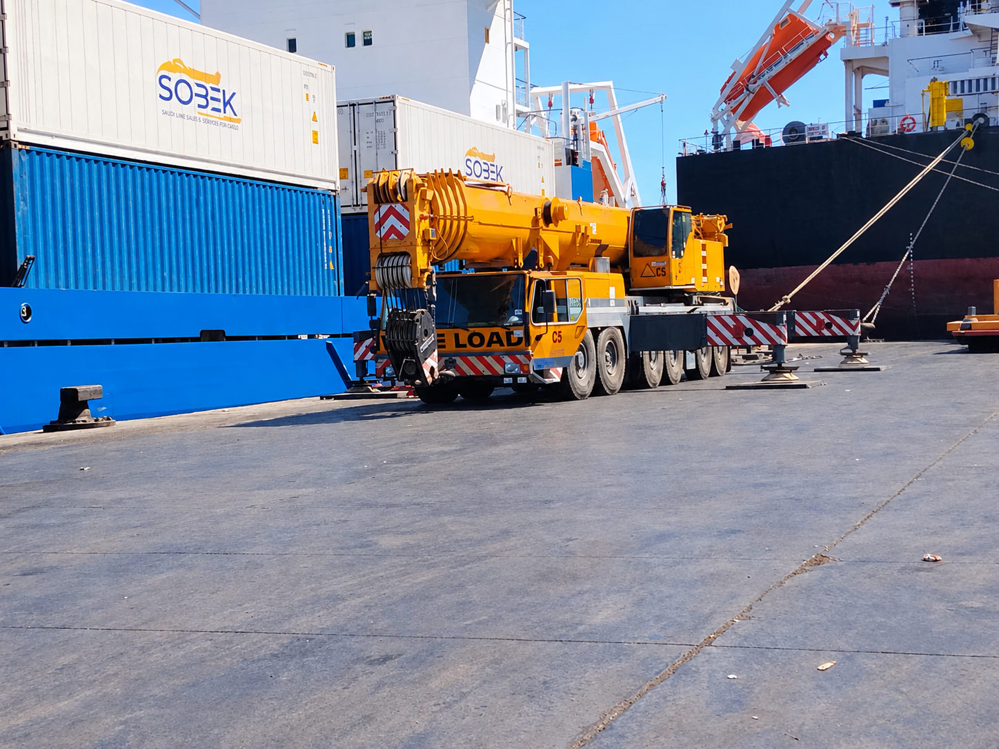 Mobile crane parked beside Sobek containers and a ship